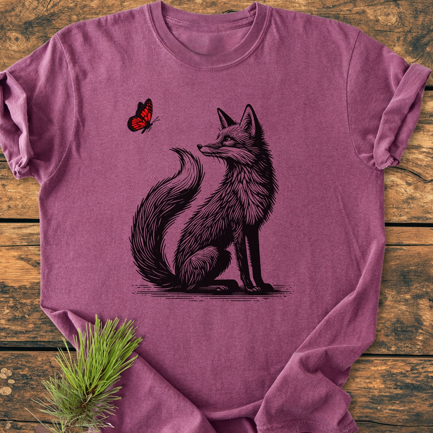 Fox And Butterfly - Vintage Wash Tee features a heathered purple design with a fox illustration and red butterfly. Laid flat, highlighting its soft, relaxed fit and durable craftsmanship on a wooden surface.