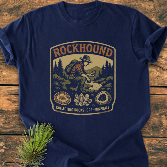 Rockhound Badge - Vintage Wash Tee featuring a hiker design and rock specimens, displayed on a wooden surface with pine. Made from soft, garment-dyed, ring-spun cotton for a relaxed fit.