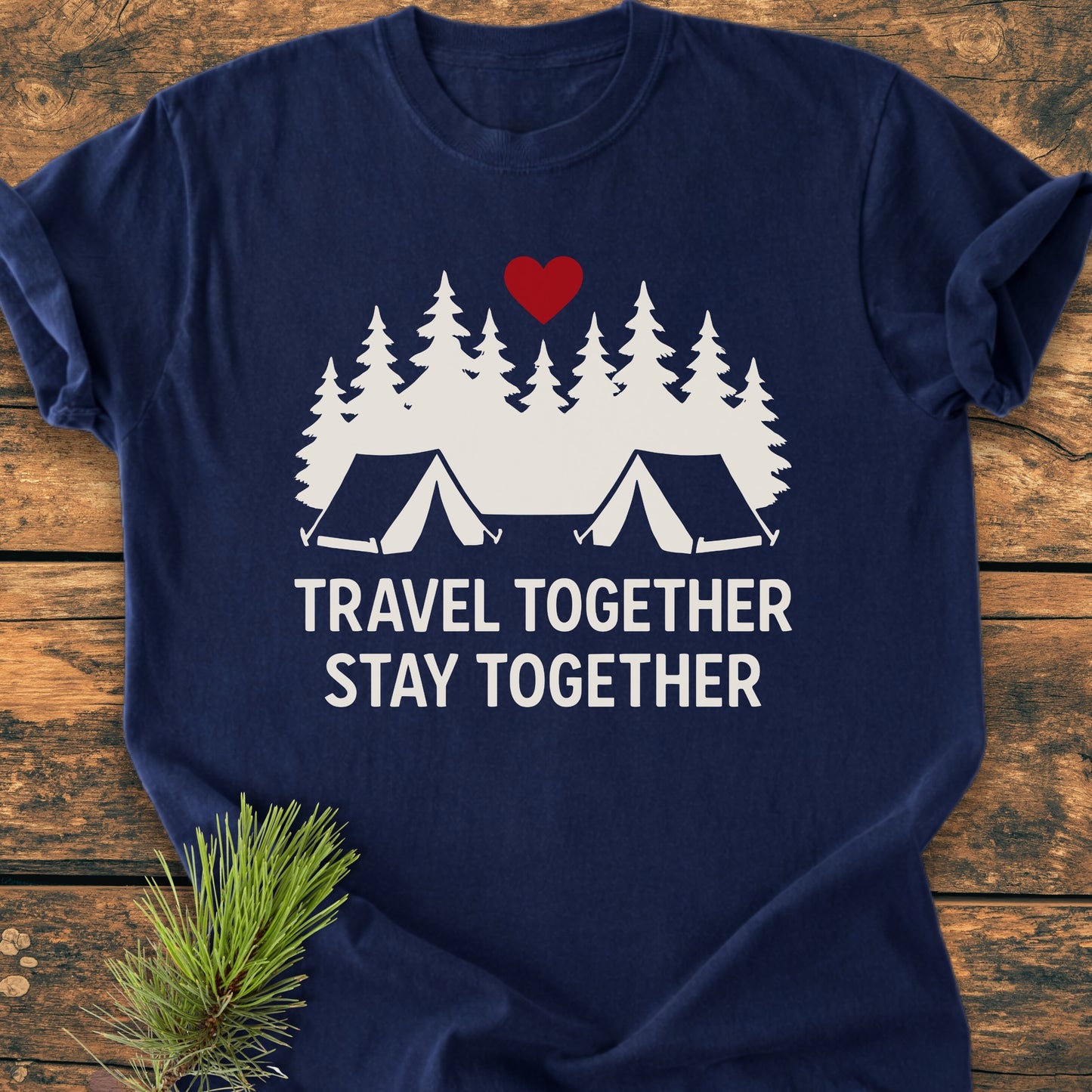 Navy-blue Travel Together Stay Together - Vintage Wash Tee featuring white pine trees, tents, and a red heart graphic. Laid flat on wood with pine sprig, highlighting its cozy, relaxed fit.
