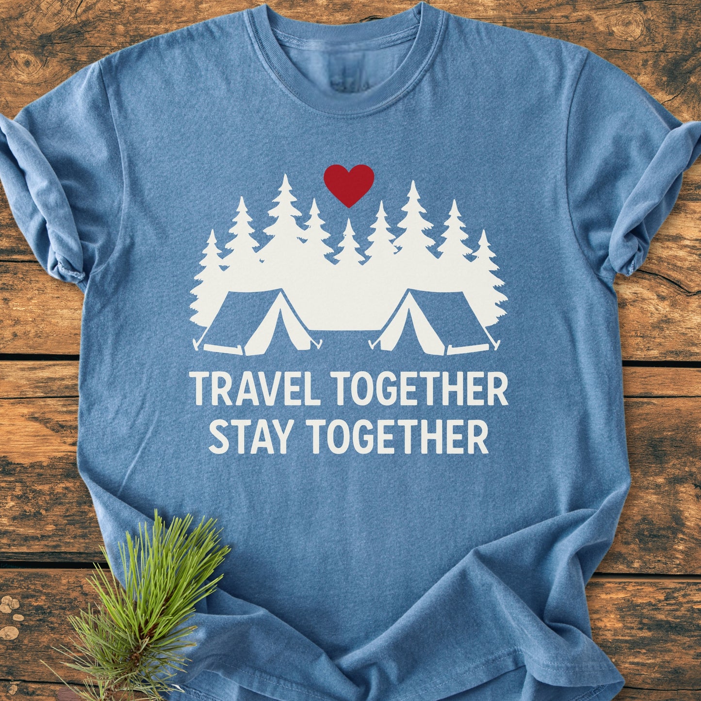 Travel Together Stay Together - Vintage Wash Tee, featuring a white graphic of pine trees and tents with a red heart, printed on a heather-blue T-shirt, displayed on a wooden surface.