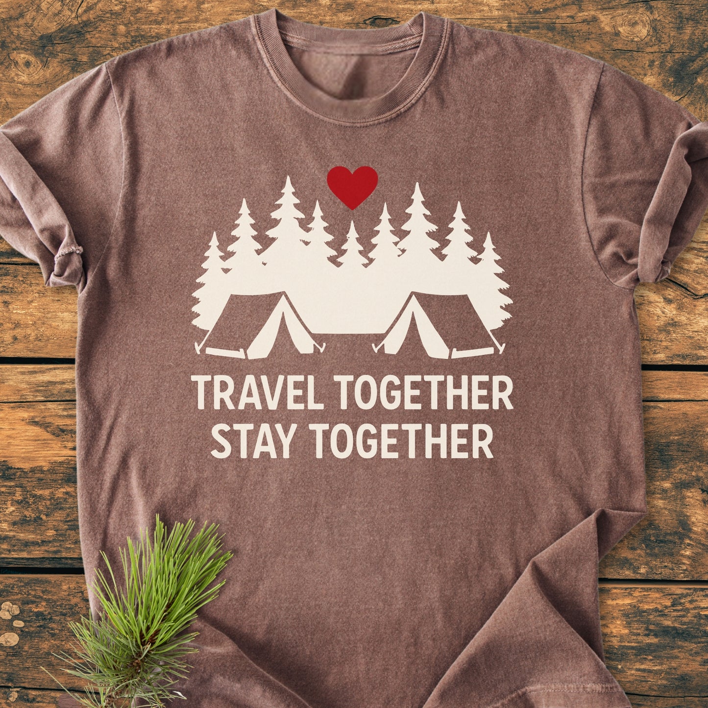 Travel Together Stay Together - Vintage Wash Tee features a simple graphic of evergreen trees and tents with a red heart, laid on wood with a pine branch accenting its cozy, relaxed design.