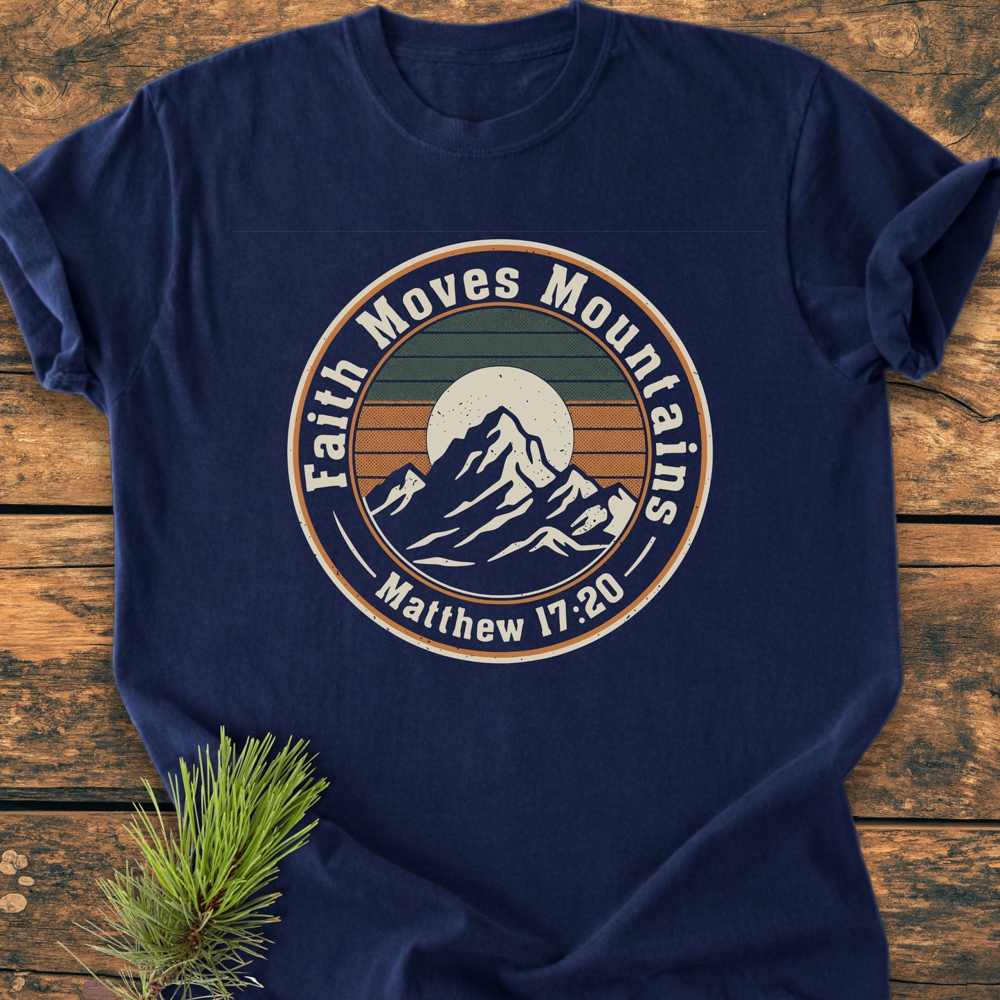 Faith Moves Mountains - Vintage Wash Tee, featuring a mountain and sun graphic with “Matthew 17:20,” laid flat on wood. The navy-blue, garment-dyed, ring-spun cotton tee exudes comfort and durability.