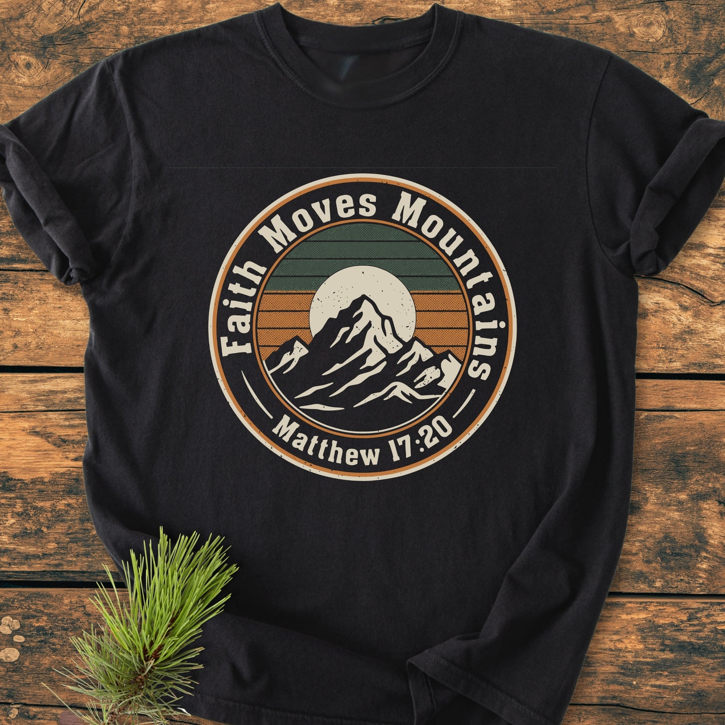 Faith Moves Mountains - Vintage Wash Tee features a circular mountain graphic with a sunset and the slogan “Faith Moves Mountains,” referencing “Matthew 17:20” on a black, soft-washed, garment-dyed T-shirt.