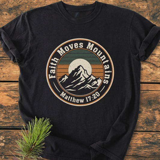 Faith Moves Mountains - Vintage Wash Tee features a circular mountain graphic with a sunset and the slogan “Faith Moves Mountains,” referencing “Matthew 17:20” on a black, soft-washed, garment-dyed T-shirt.