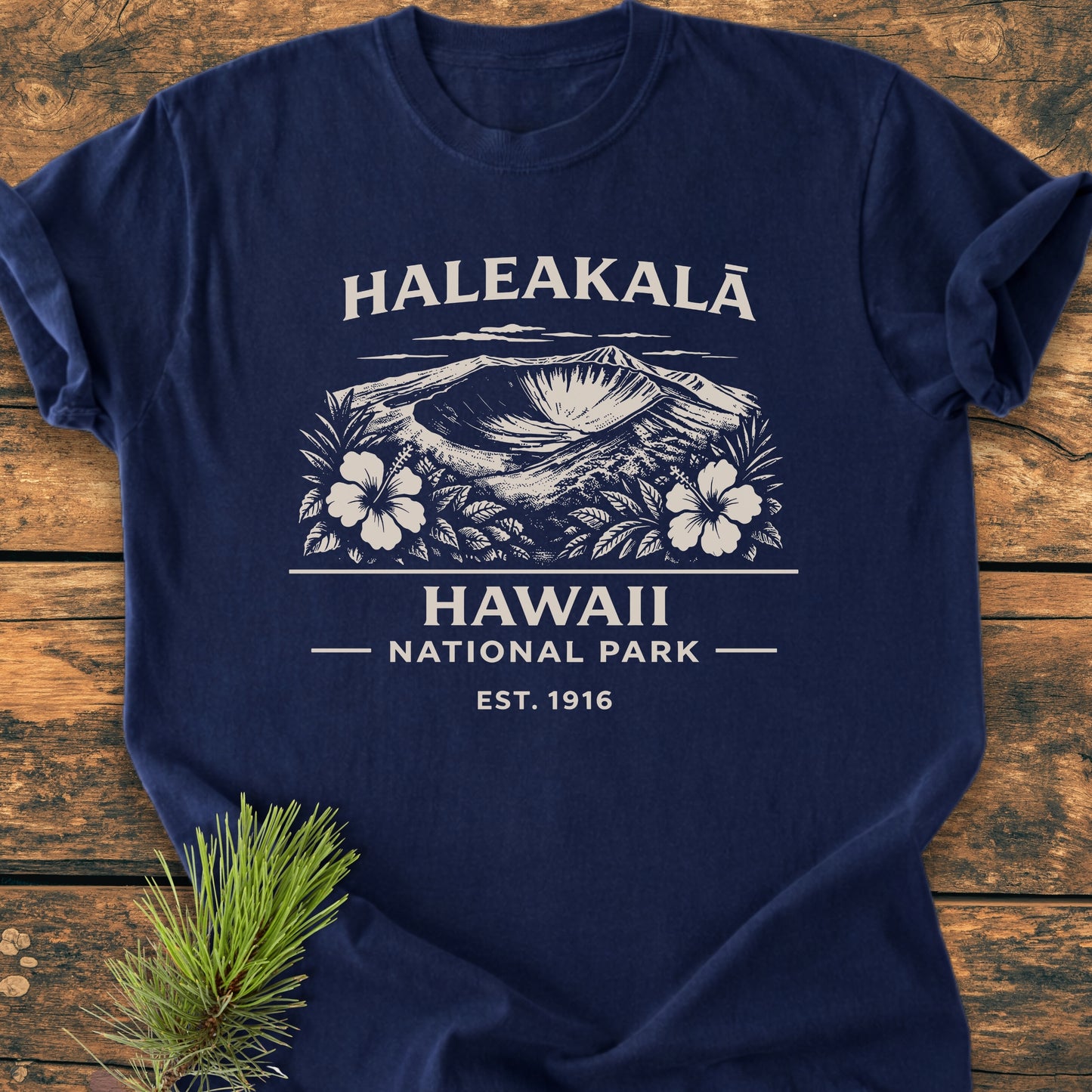Haleakalā Hawaii National Park - Vintage Wash Tee features a volcanic crater with hibiscus print, HALEAKALĀ text, and park details. Displayed on wood, includes a pine sprig prop.