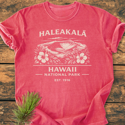 Haleakalā Hawaii National Park - Vintage Wash Tee featuring a salmon-tone, white illustrated crater with hibiscus, and text. Laid on wood, pine sprig beside. Cozy, relaxed fit, 100% ring-spun cotton.