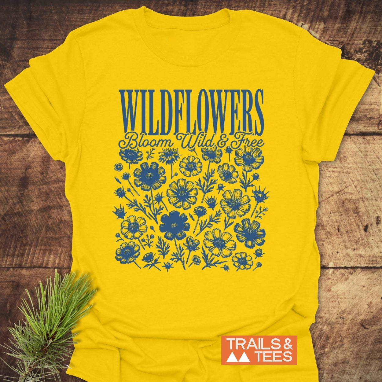 Wildflowers Bloom Wild And Free T-Shirt featuring hand-drawn wildflower illustrations and text in blue. Designed by Trails & Tees, it's crafted from soft cotton for comfort and durability.