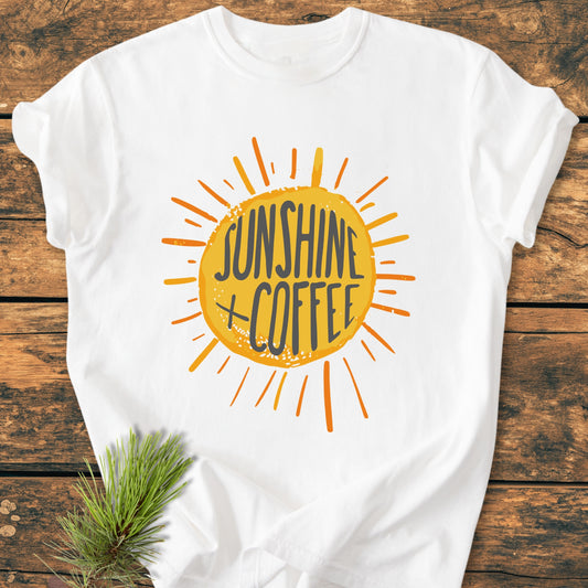 Sunshine + Coffee - Vintage Wash Tee on wooden surface, featuring a yellow sunburst design with dark text. T-shirt is soft-washed, relaxed fit, and made from 100% ring-spun cotton.