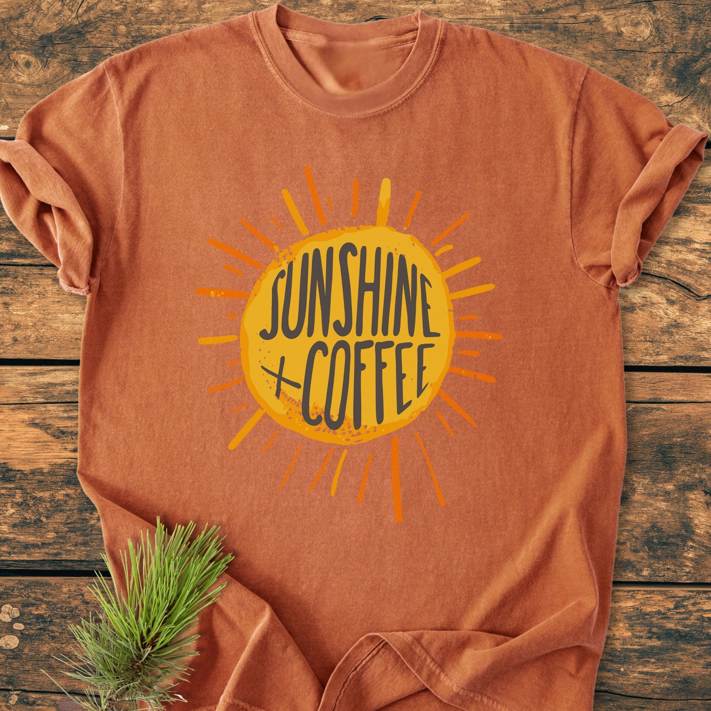 Sunshine + Coffee - Vintage Wash Tee: Rust-orange, short-sleeve with a yellow sunburst graphic, laid flat on wood. Features garment-dyed, pre-shrunk cotton, relaxed fit, and durable double-needle stitching.