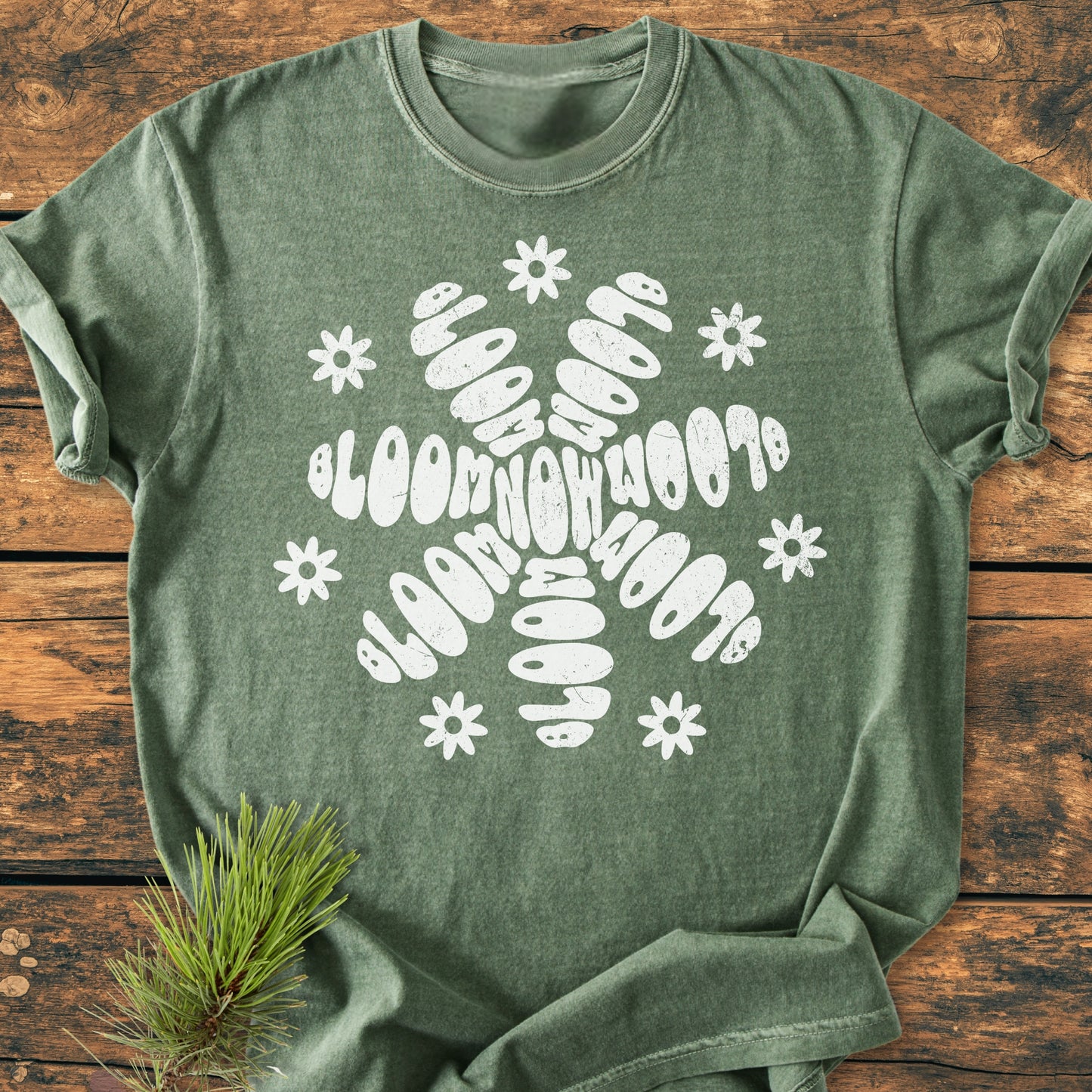Bloom Now - Vintage Wash Tee featuring a unique white “BLOOM NOW” petal graphic with daisy accents, displayed on a rustic surface, highlighting its relaxed, durable design and soft, garment-dyed fabric.