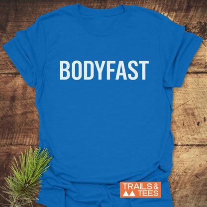 Bright blue BODYFAST T-Shirt with bold white lettering, styled with a pine sprig and orange TRAILS & TEES logo, symbolizing energy, balance, and a healthier lifestyle.