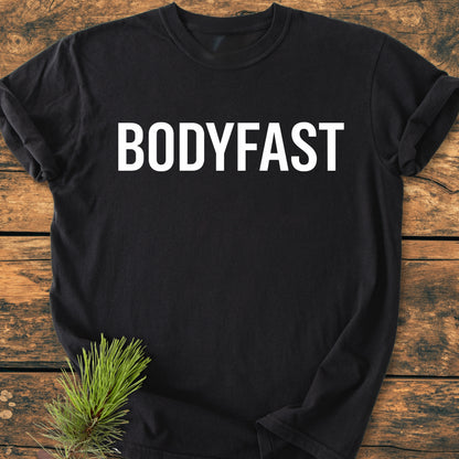 BODYFAST - Vintage Wash Tee on a rustic wooden surface, featuring bold white BODYFAST lettering. Pine needles add a natural touch, emphasizing the lifestyle of energy and balance.