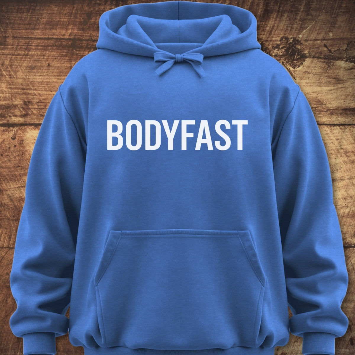 BODYFAST Hoodie laid on wood, featuring large white lettering, a front pouch pocket, and drawstring hood. Its relaxed, unisex fit and garment-dyed fabric offer trail-tested comfort.