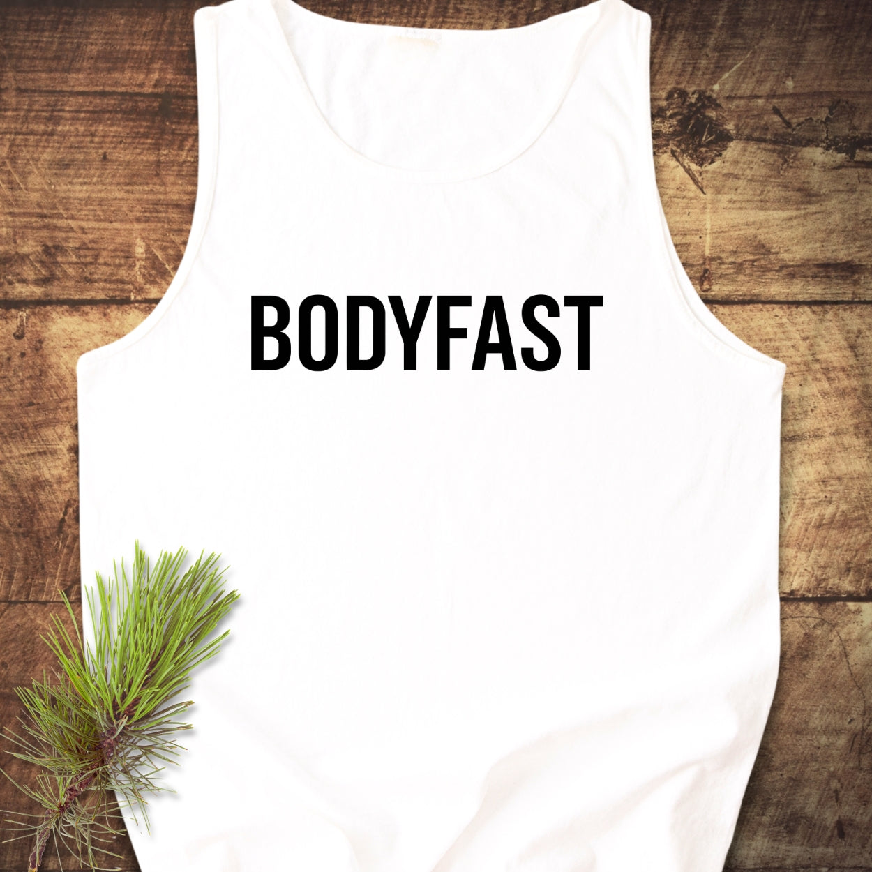 BODYFAST Tank Top features a plain white, sleeveless design laid flat, showcasing bold black branding across the chest. Made from sustainable 100% ring-spun US cotton, it offers a relaxed fit.