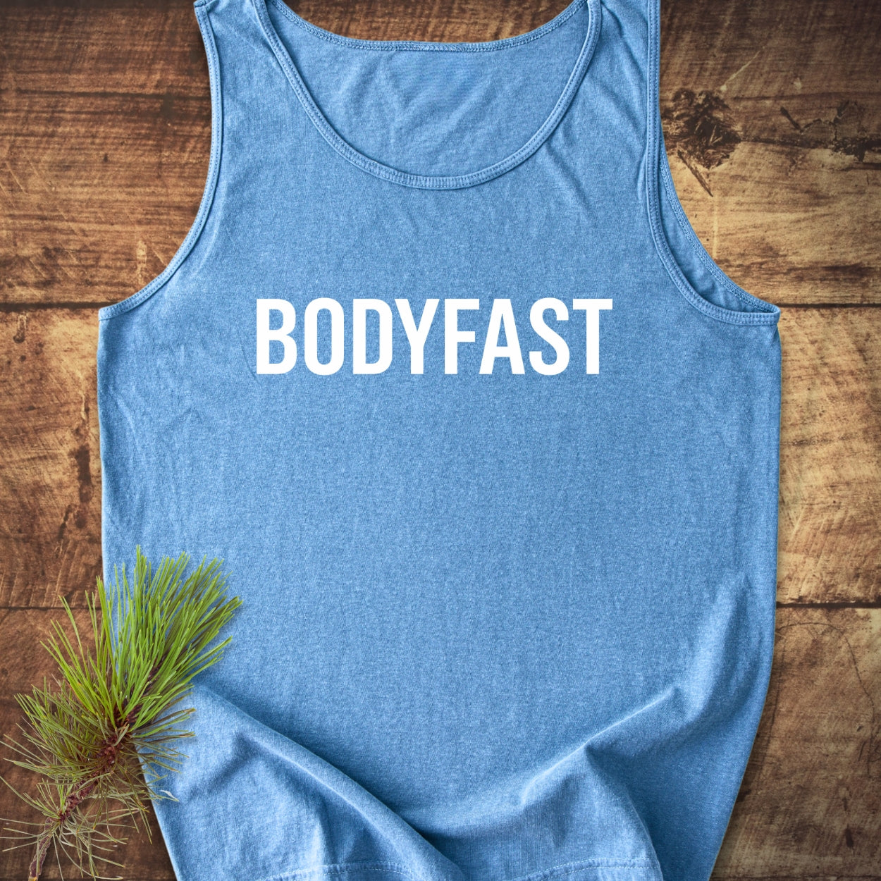 BODYFAST Tank Top displayed on wood, showcasing its relaxed fit and bold white lettering. Made from 100% US cotton, it embodies sustainable fashion with its ethically produced, eco-friendly materials.