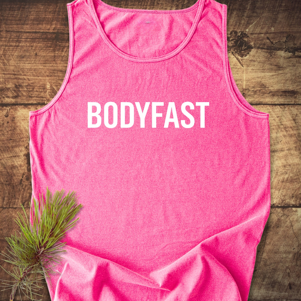BODYFAST Tank Top; pink, sleeveless, laid flat with bold white lettering. Features a relaxed fit, made from 100% ring-spun US cotton, adorned with a small pine sprig for a natural touch.