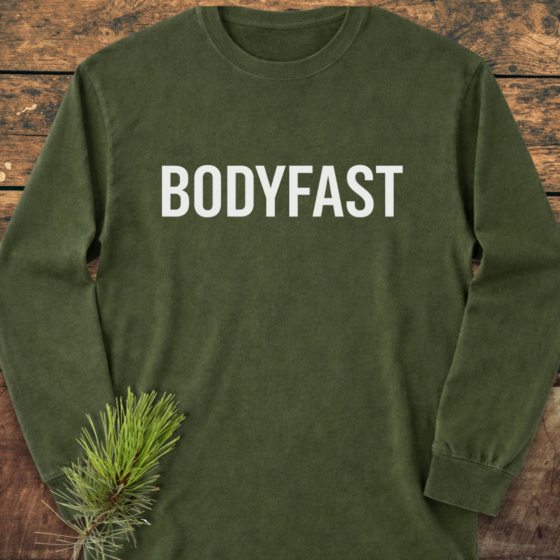 BODYFAST Long-Sleeve Tee in olive-green, features BODYFAST in bold white on the chest, with a pine-branch accent. Made of 100% ring-spun cotton for softness and a relaxed fit.
