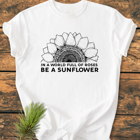 Be A Sunflower - Vintage Wash Tee features a black sunflower line-drawing and slogan on a white T-shirt, laid flat on wood, with a pine sprig accent.