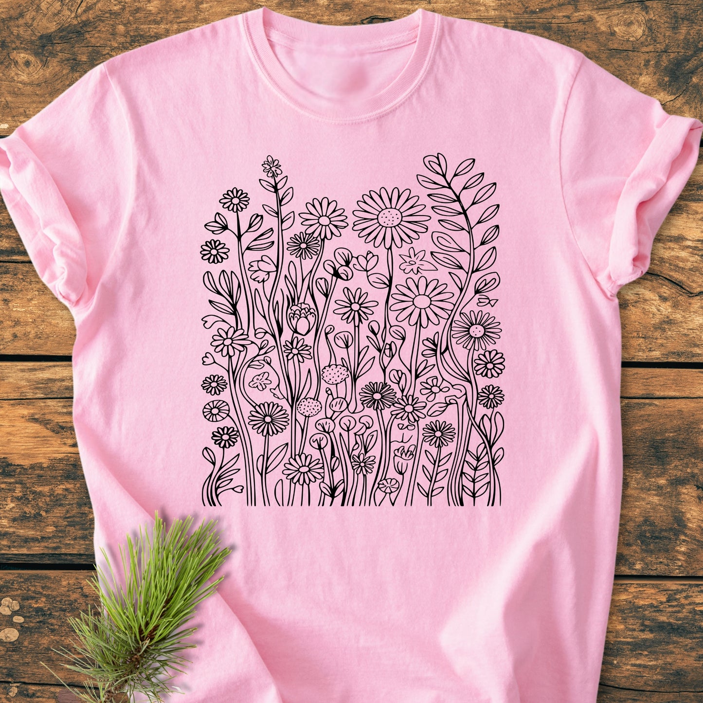 Wildflower Trails - Vintage Wash Tee in pastel-pink, featuring a black hand-drawn wildflower illustration on the chest, laid flat on wood with a pine sprig for styling.