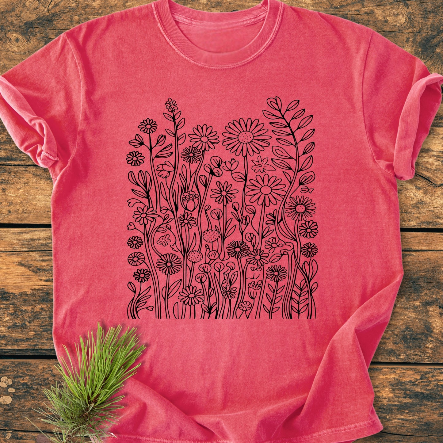 Wildflower Trails - Vintage Wash Tee, a soft, faded-rose T-shirt with black wildflower illustration, lies on rustic wood, showcasing its relaxed fit, garment-dyed comfort, and durable stitching.