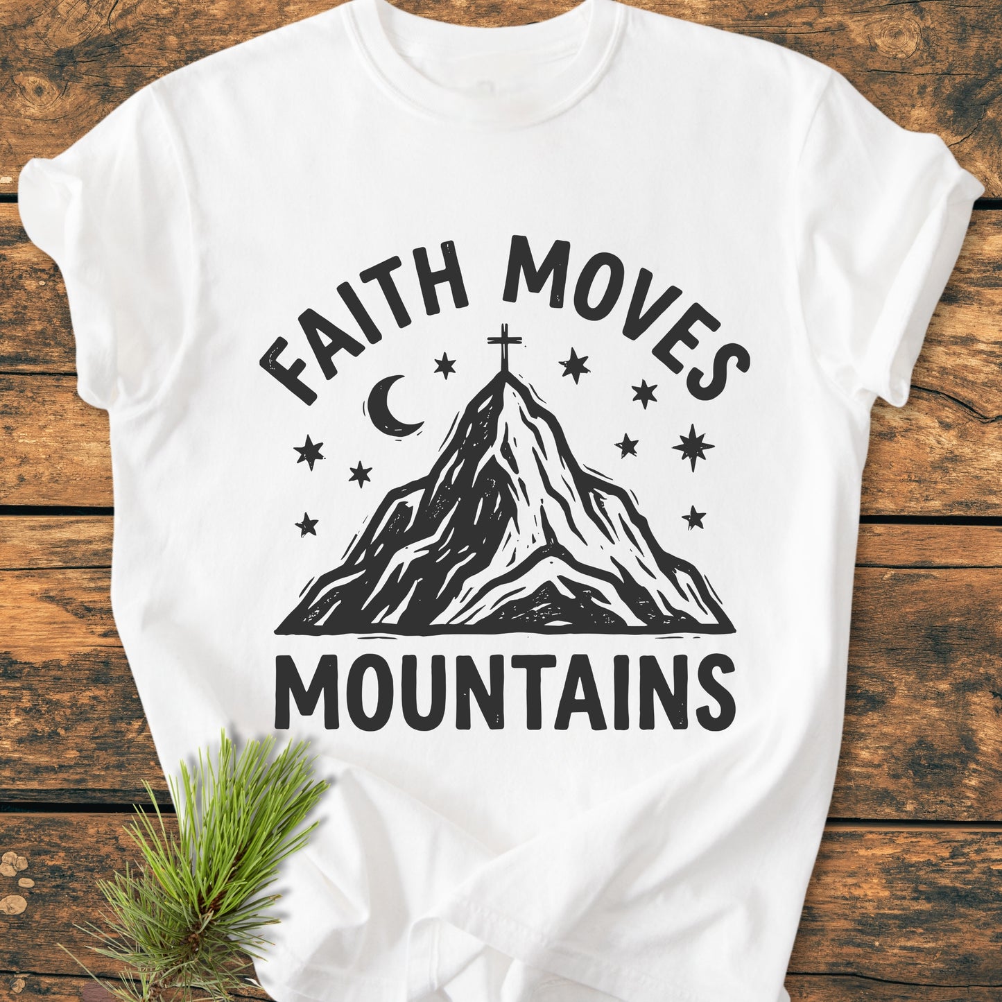 Faith Moves Mountains - Vintage Wash Tee featuring a stylized mountain with a cross, stars, and crescent moon, laid on wood. Made from 100% ring-spun cotton for comfort and durability.