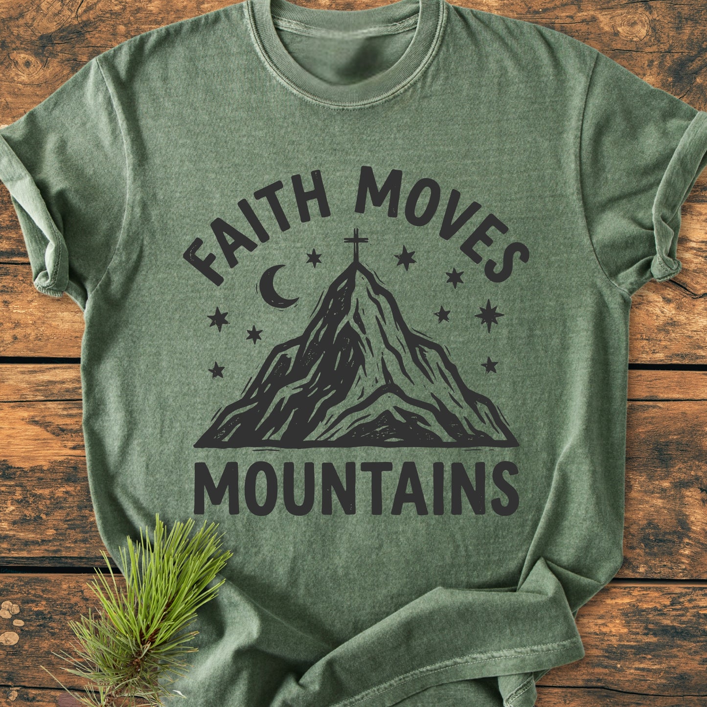 Heather-green Faith Moves Mountains - Vintage Wash Tee on wooden surface, featuring a mountain peak graphic with a cross, stars, crescent moon, and slogan. Soft, durable, and relaxed fit, ideal for daily wear.
