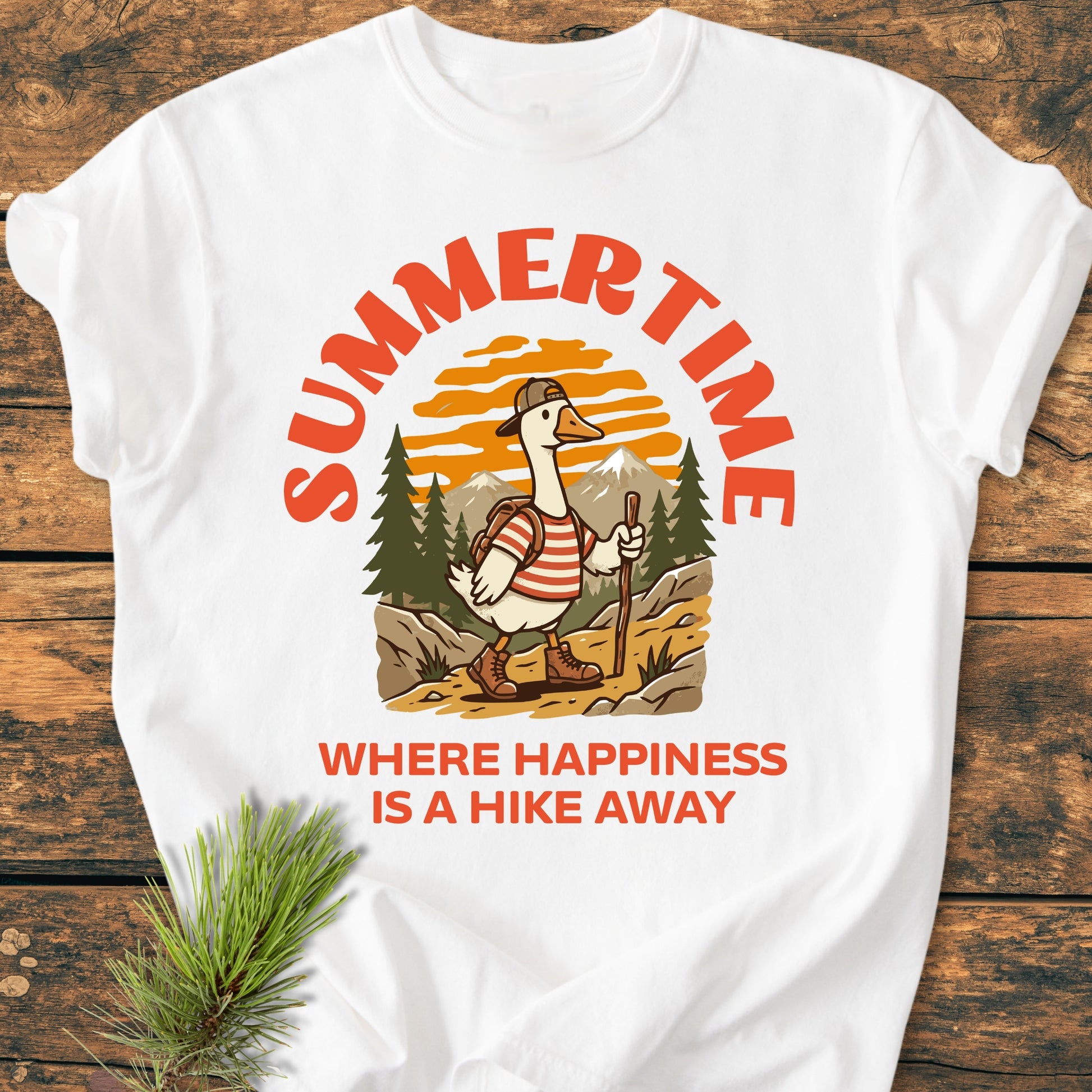 Summertime Hike - Vintage Wash Tee featuring a cartoon hiking goose in vibrant gear, surrounded by nature. Displayed on a wooden surface, highlighting its relaxed fit and cozy garment-dyed fabric.