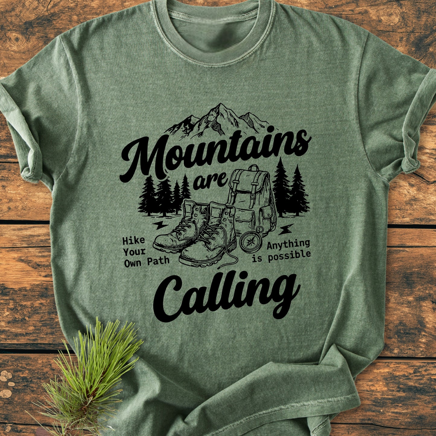 Heather-green Cute Mountains Are Calling Illustration - Vintage Wash Tee features a black outdoors-themed graphic with mountains, pine trees, hiking boots, backpack, compass, and motivating slogans, perfect for outdoor enthusiasts.