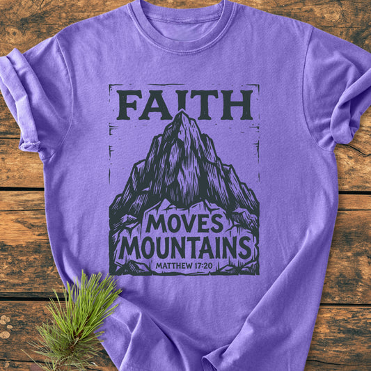 Faith Moves Mountains - Vintage Wash Tee featuring a black mountain design with FAITH MOVES MOUNTAINS and Matthew 17:20, displayed on a wooden surface with a pine sprig nearby.