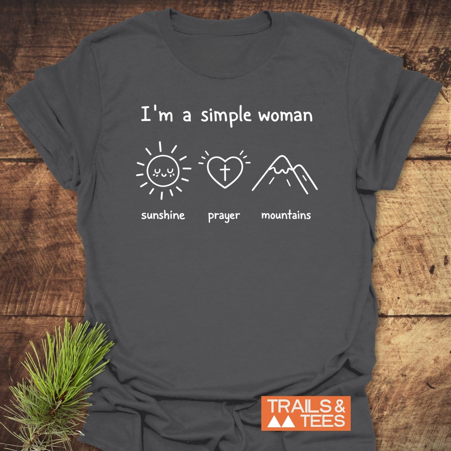 A Simple Woman - Sunshine Prayer Mountains T-Shirt: Charcoal-gray tee with icons of a sun, heart-cross, and mountains. Logo “TRAILS & TEES” in corner. Made for outdoor enthusiasts.