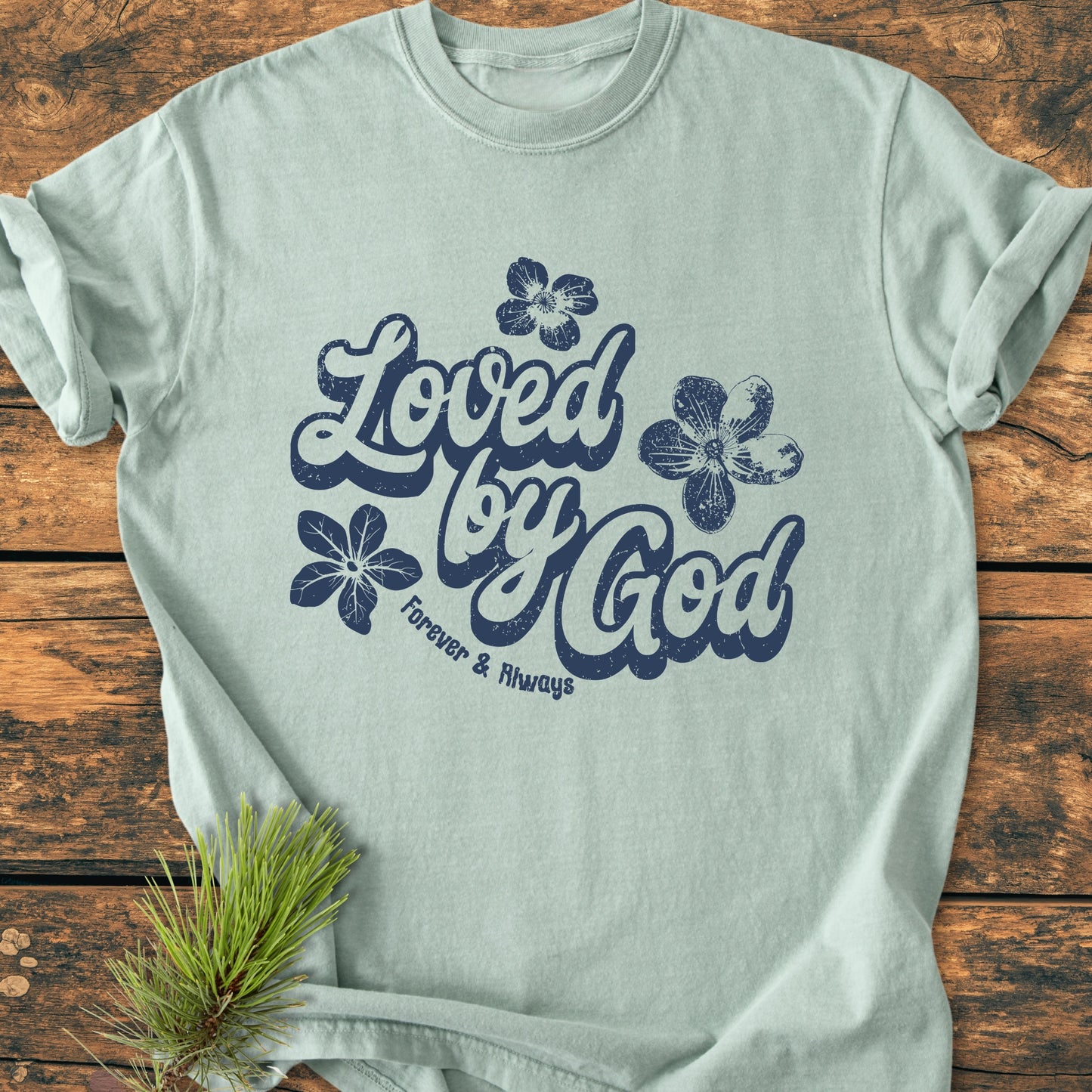 Loved By God - Vintage Wash Tee in light-seafoam green features navy “Loved by God” graphic with flowers, offering a cozy, relaxed fit. Made from soft, pre-shrunk 100% ring-spun cotton.