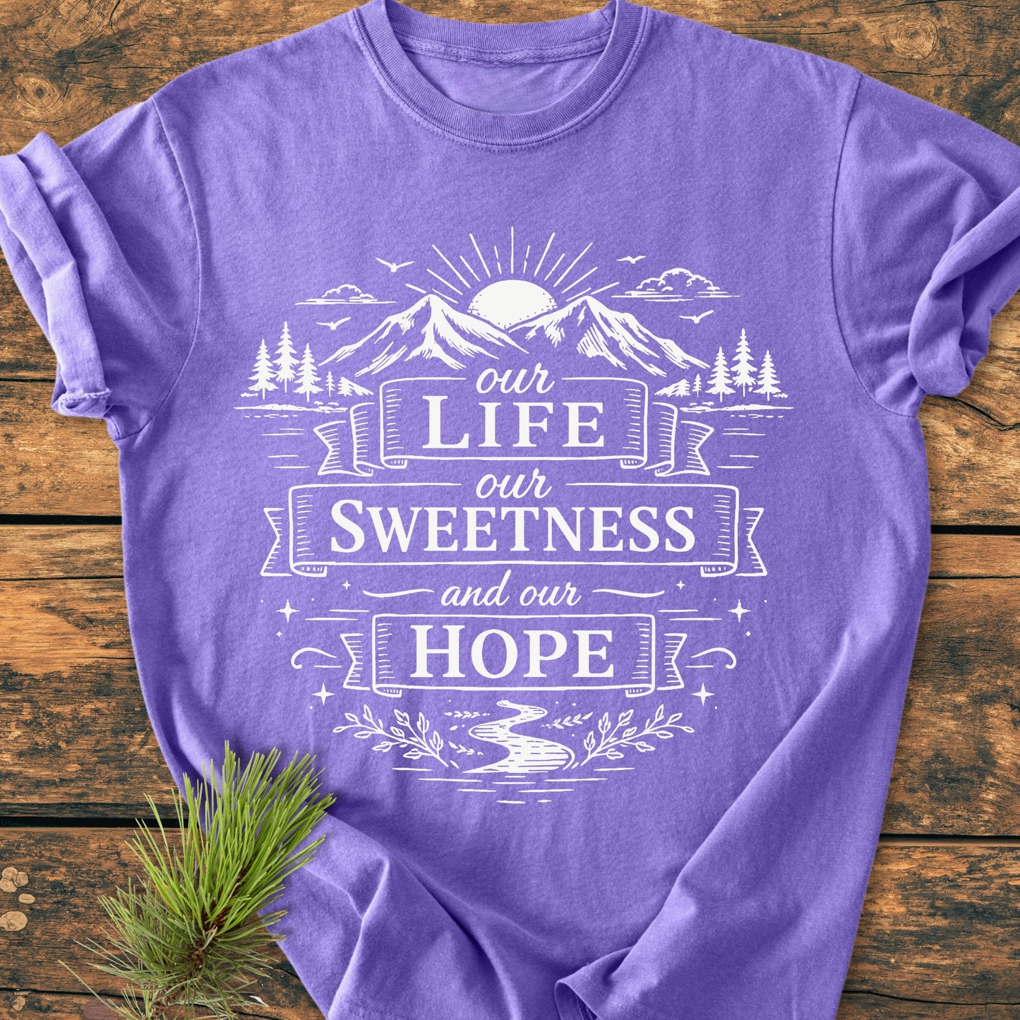 Our Life, Our Sweetness, Our Hope - Vintage Wash Tee: Lavender T-shirt with white nature scene and quote, laid on wood. Features mountains, sun, trees, stream; relaxed fit, soft-washed, durable fabric.