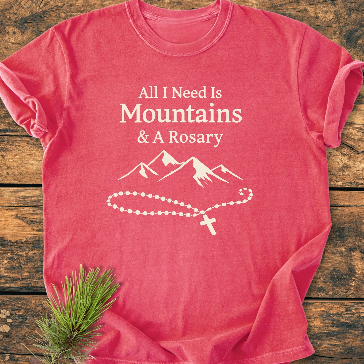 Coral-pink All I Need Is Mountains And A Rosary - Vintage Wash Tee with mountain-rosary graphic, laid on wood. Features garment-dyed, pre-shrunk, ring-spun cotton for comfort and durability.