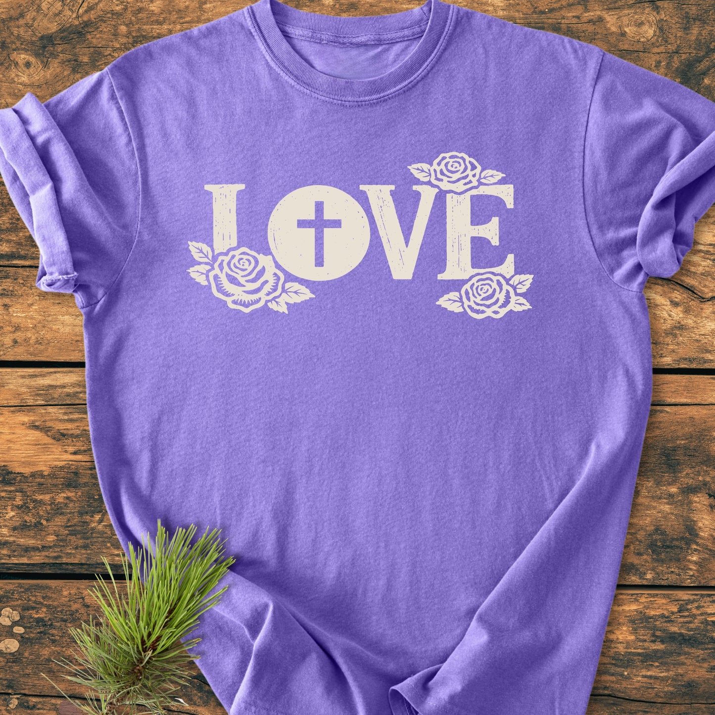 LOVE – Eucharistic Faith - Vintage Wash Tee: Lavender-purple T-shirt with “LOVE” text, featuring a cross and rose accents, laid flat with a pine sprig beside it, showcasing its relaxed, soft-washed design.