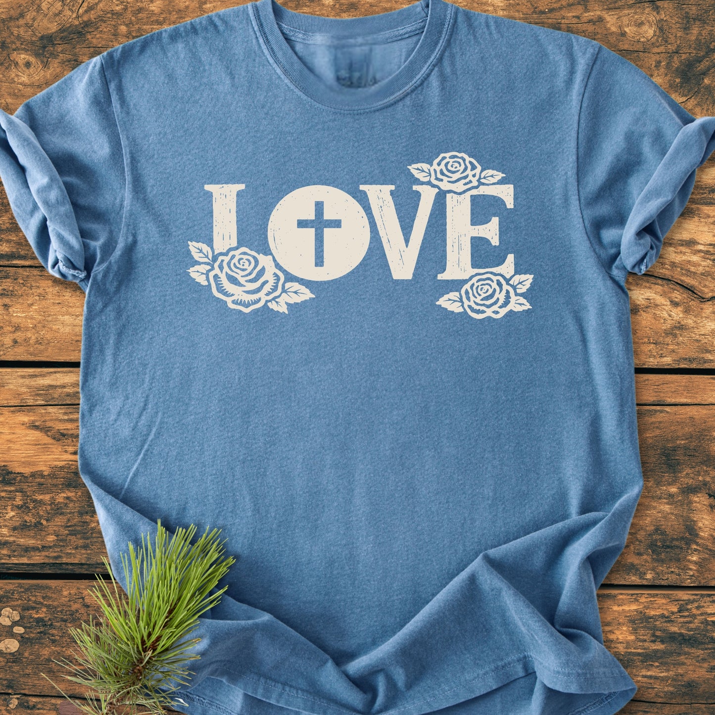 LOVE – Eucharistic Faith - Vintage Wash Tee: Heather-blue T-shirt with LOVE text, featuring a cross in the O and rose motifs. Laid flat with pine sprig accent, showcasing a cozy, relaxed fit.