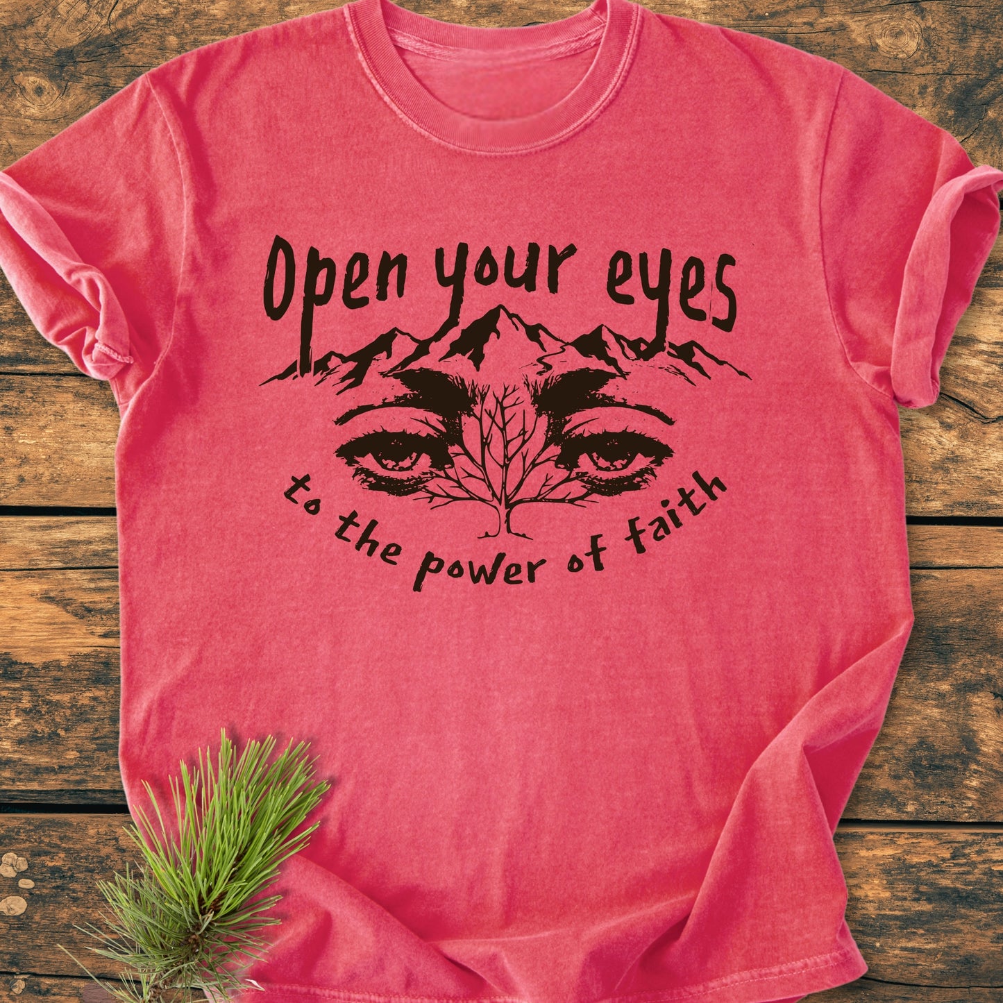 Open Your Eyes To The Power Of Faith - Vintage Wash Tee: Coral T-shirt with mountain and eyes graphic, slogan above and below. Laid on rustic wood, pine sprig beside. Comfortable, durable, customizable design.