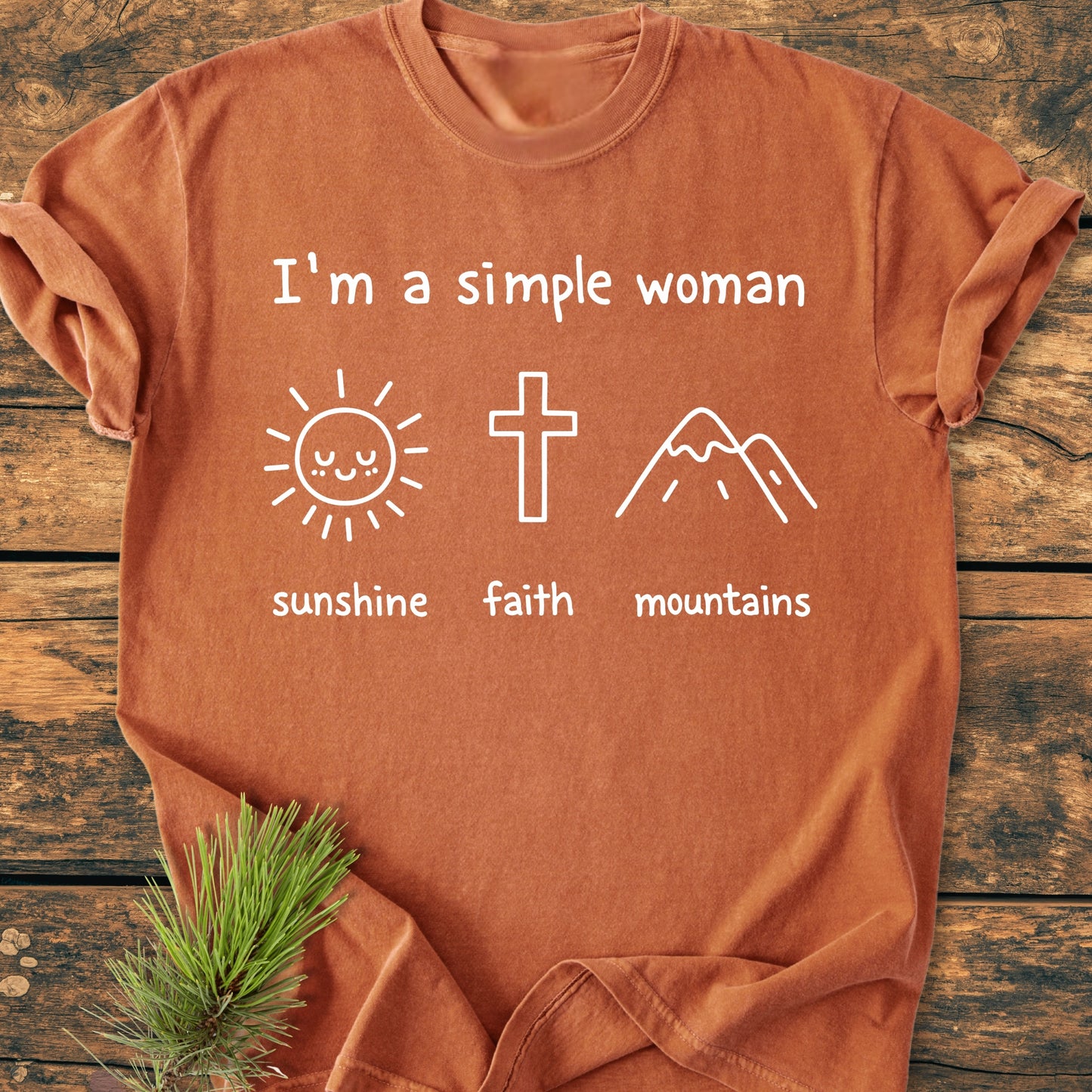 I'm A Simple Woman. Sunshine Faith Mountains - Vintage Wash Tee on wooden surface, featuring white line-drawings of a sun, cross, and mountains. Soft-washed, 100% ring-spun cotton, relaxed fit.