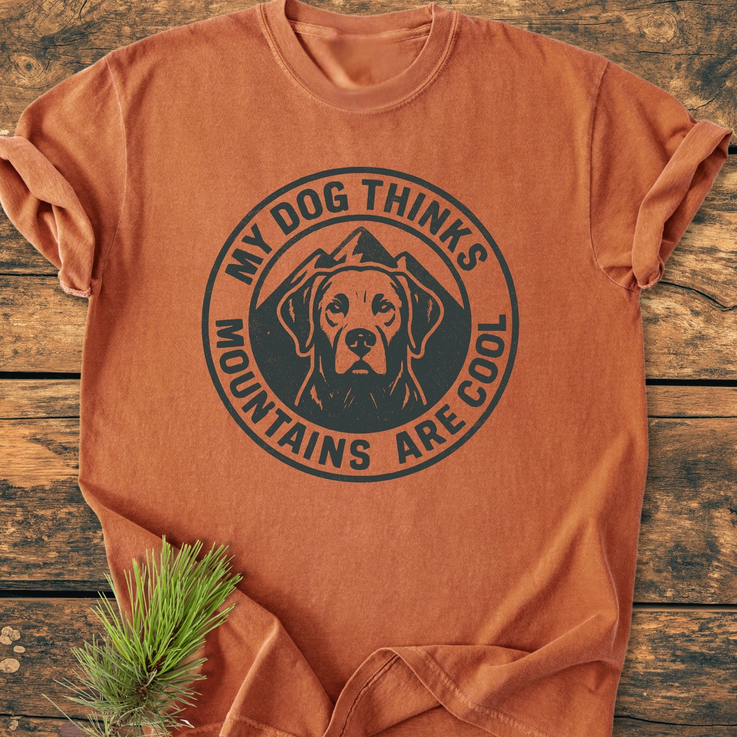 My Dog Thinks Mountains Are Cool - Vintage Wash Tee featuring a dog and mountain graphic, laid flat with a pine sprig. Soft, relaxed fit, rust-orange, garment-dyed, 100% ring-spun cotton.