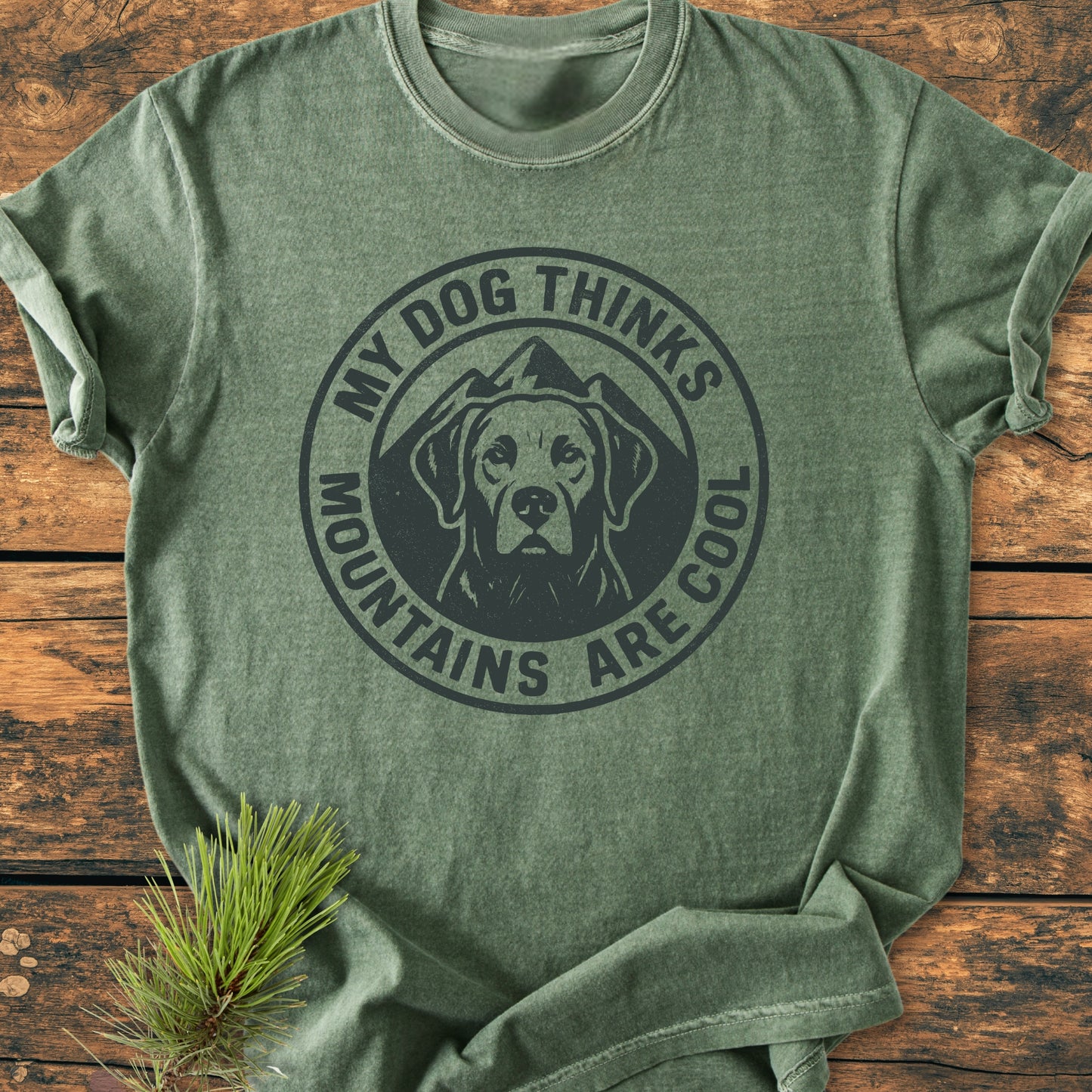 Olive-green My Dog Thinks Mountains Are Cool - Vintage Wash Tee featuring a dog head graphic with mountains, laid on wood with pine sprig; made of soft, durable, ring-spun cotton for comfort.