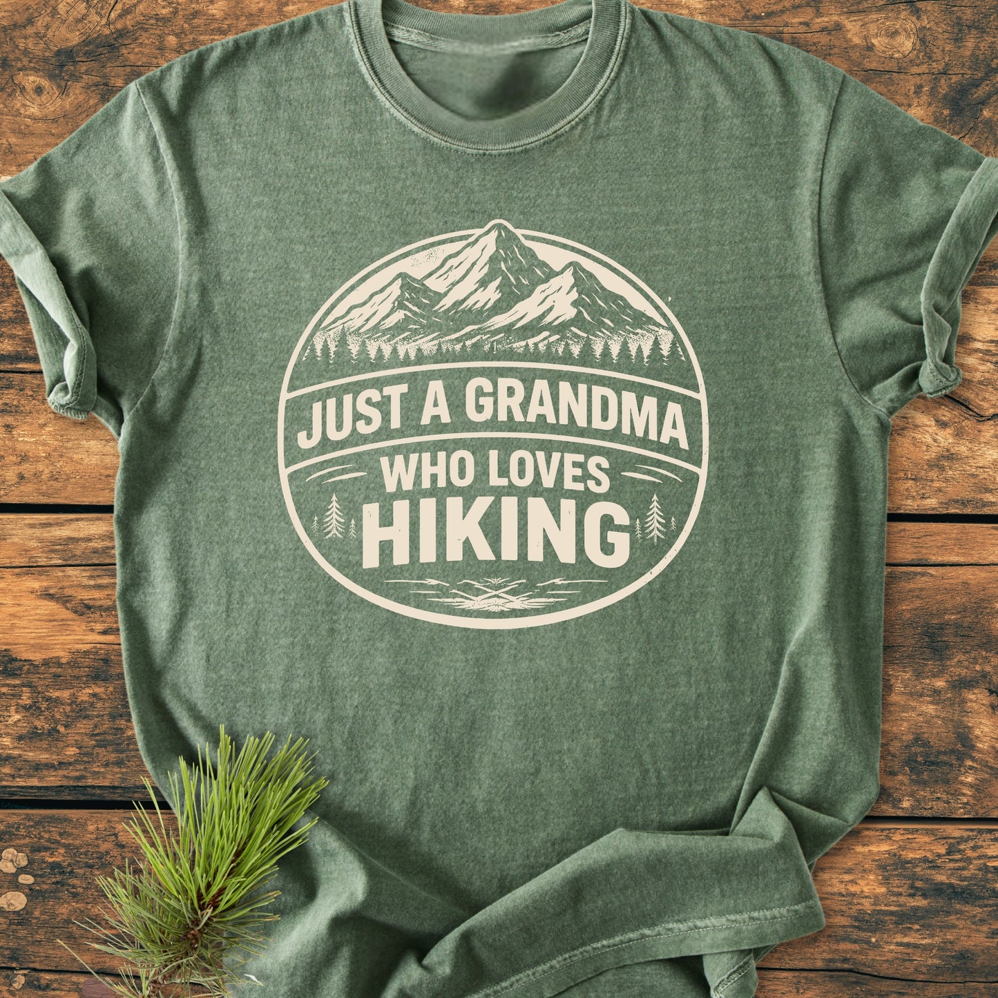 Heather-green Just A Grandma Who Loves Hiking - Vintage Wash Tee with mountain and pine graphic, laid flat. Features soft, garment-dyed cotton for comfort and durability, ideal for outdoor enthusiasts.