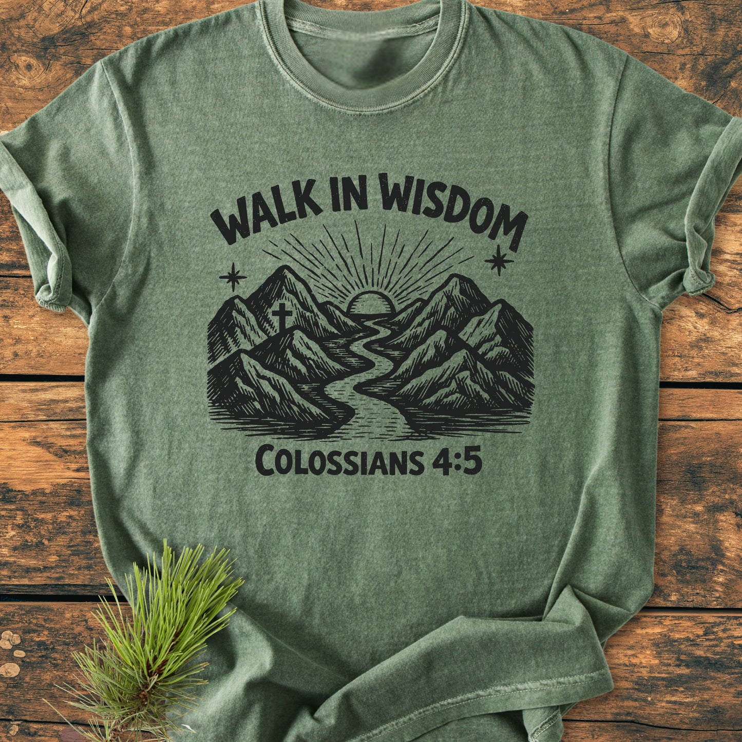 Walk In Wisdom, Colossians 4:5 - Vintage Wash Tee featuring a mountain and river graphic with a sun, laid flat on wood, highlighting its soft, relaxed fit and durable craftsmanship.
