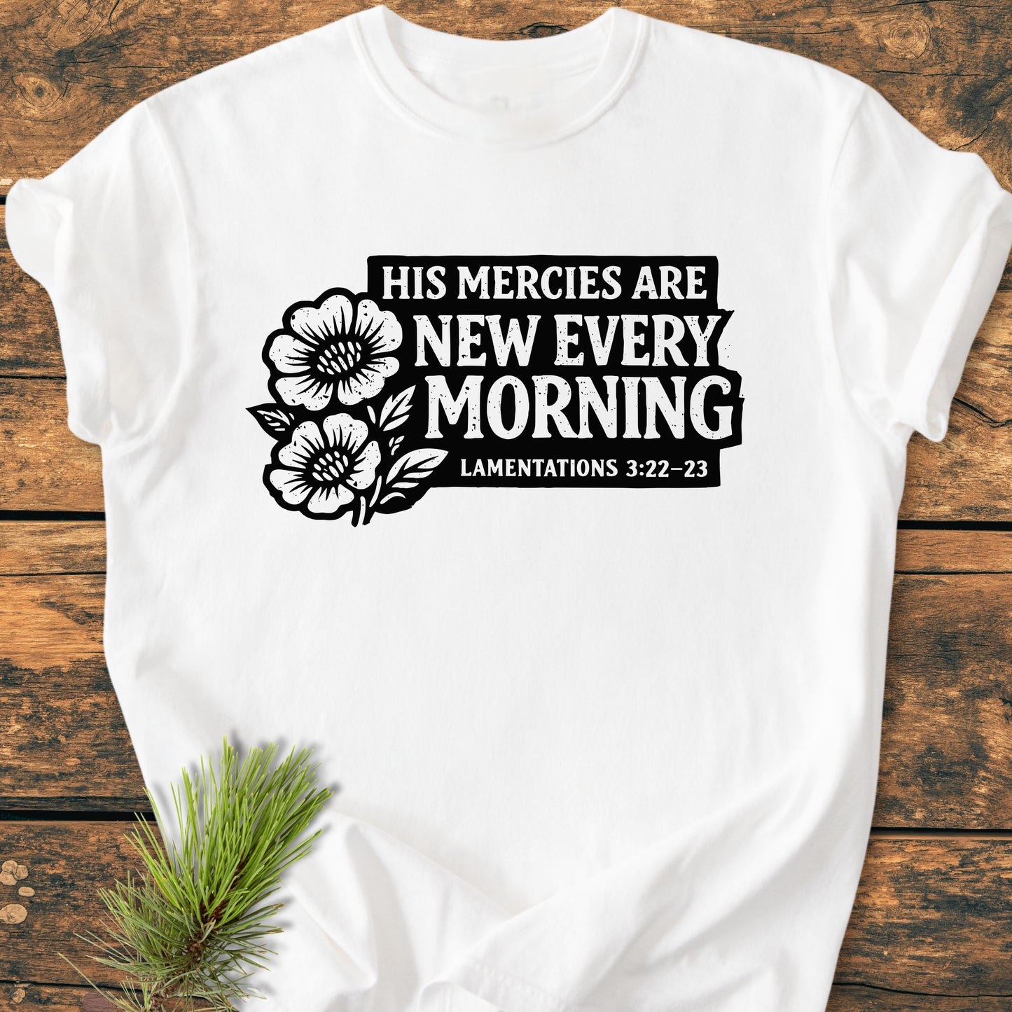 New Every Morning Lamentations 3:22-23 - Vintage Wash Tee features a black quote and floral graphic on a white T-shirt, laid on wood, with a pine sprig accent.