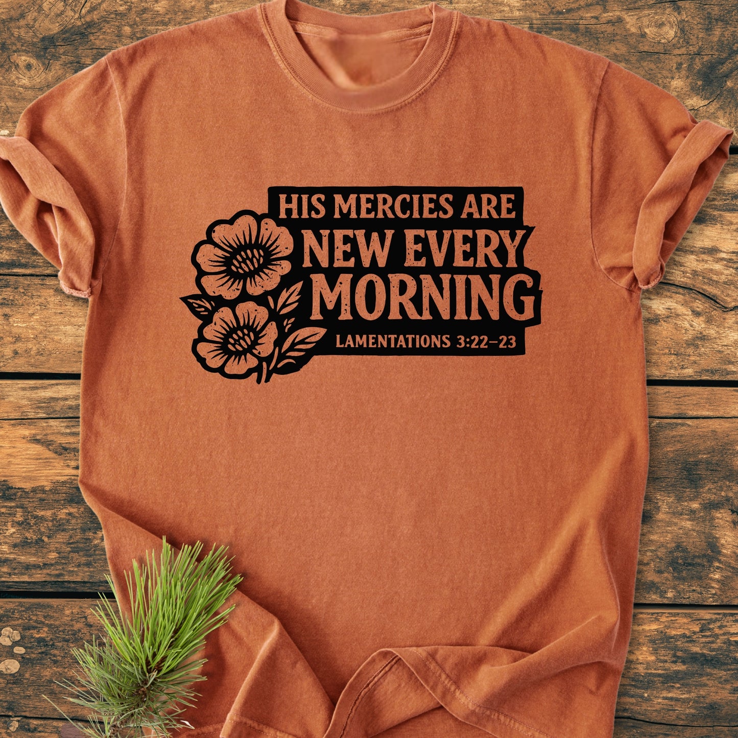New Every Morning Lamentations 3:22-23 - Vintage Wash Tee, featuring a bold floral graphic and text, displayed on a wooden surface with a pine sprig, showcasing its relaxed, durable design.