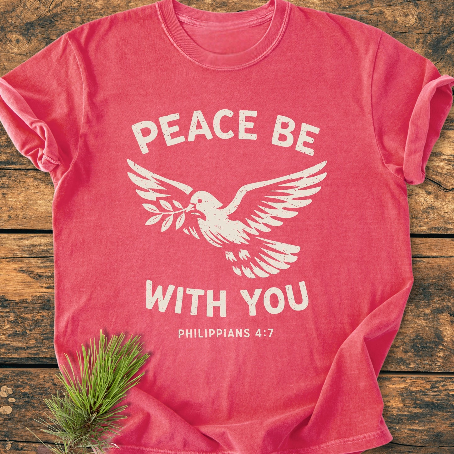 Red-pink Peace Be With You Philippians 4:7 - Vintage Wash Tee featuring a dove with olive branch, text in white, and pine sprig beside it, showcasing its relaxed fit and durability.