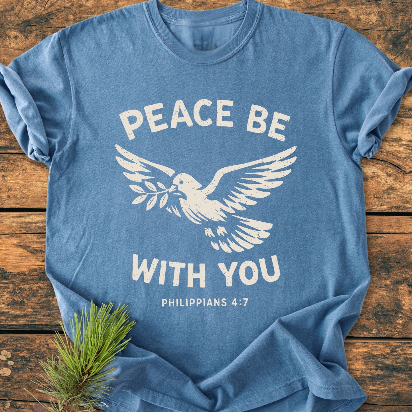 Peace Be With You Philippians 4:7 - Vintage Wash Tee features a soft-blue color with a white dove and scripture design, laid on wood. Enhanced durability and comfort with a relaxed, pre-shrunk fit.