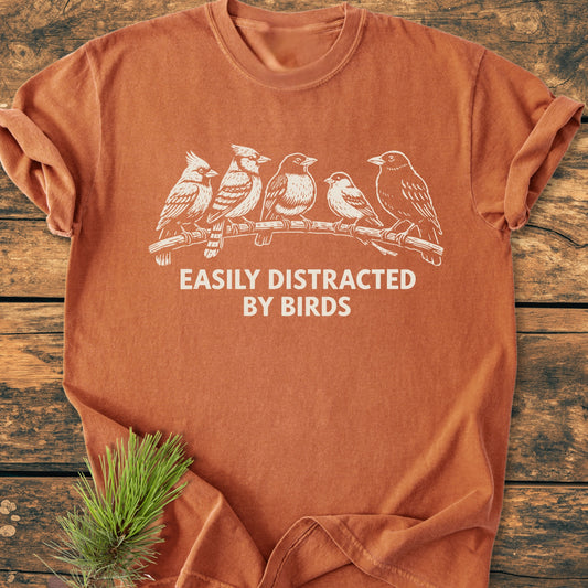 Easily Distracted By Birds - Vintage Wash Tee: Rust-orange, short-sleeve T-shirt with five birds design and slogan, laid flat on wood, highlighting its relaxed, cozy fit and durable, garment-dyed fabric.