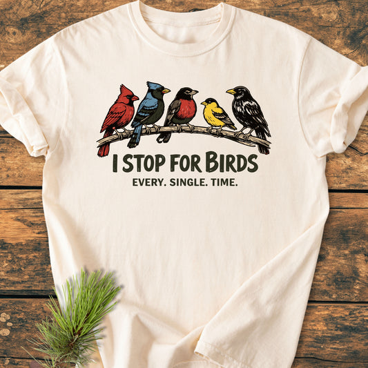 I Stop For Birds - Vintage Wash Tee features five illustrated birds on a branch with bold slogans, laid on a wooden surface, showcasing its relaxed fit and off-white, garment-dyed fabric.