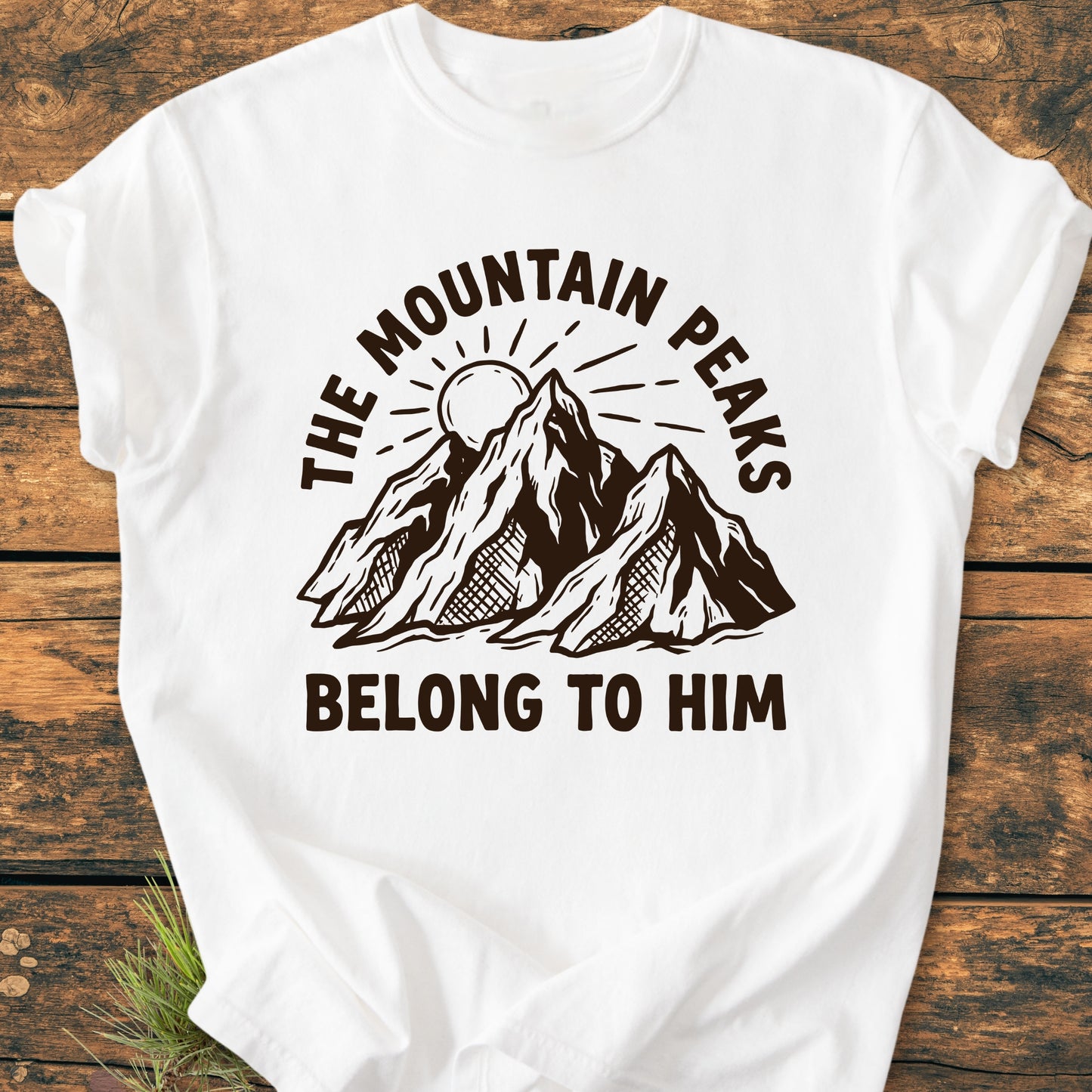 The Mountain Peaks Belong To Him - Vintage Wash Tee features a brown-ink mountain illustration with a sun, surrounded by bold text, on a laid-flat white T-shirt, highlighting its relaxed fit and durability.