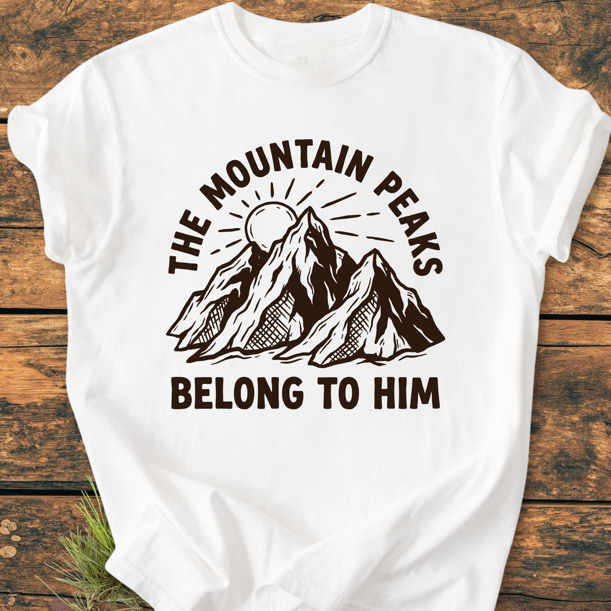 The Mountain Peaks Belong To Him - Vintage Wash Tee features a brown-ink mountain illustration with a sun, surrounded by bold text, on a laid-flat white T-shirt, highlighting its relaxed fit and durability.