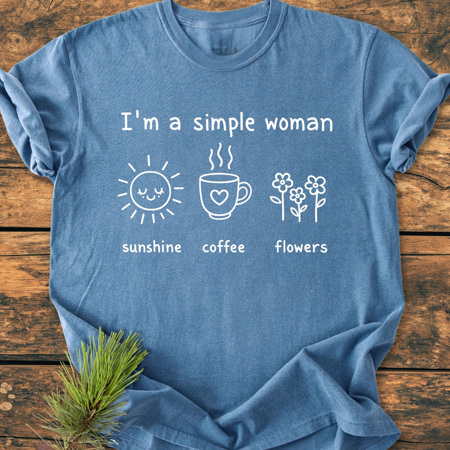 I'm A Simple Woman. Sunshine Coffee Flowers - Vintage Wash Tee on wood surface, featuring a white hand-drawn style design with icons of a sun, coffee mug, and flowers, exuding casual comfort.